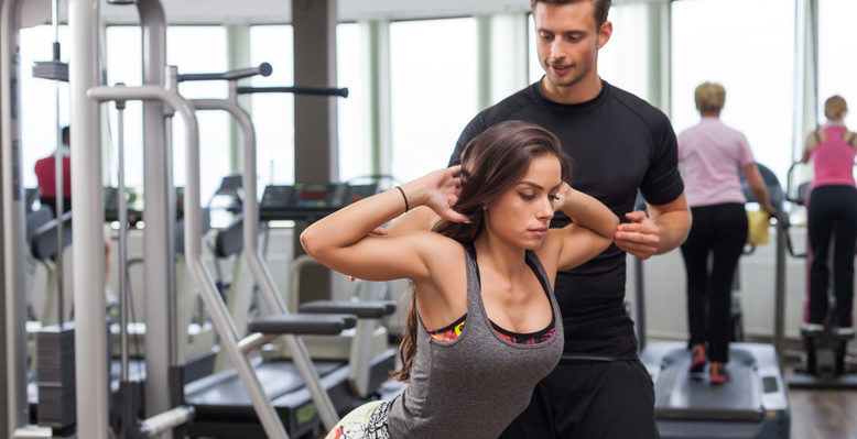 woman with personal trainer flexing muscles in gym